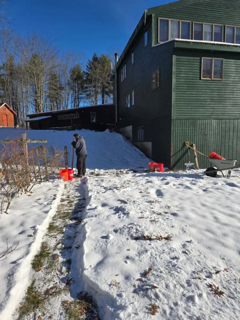 Worker digging fence post holes in winter snow